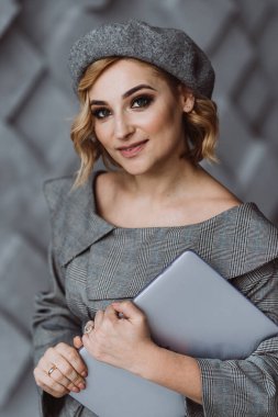 Güzel, zeki, sevimli, çekici, zarif iş kadını elinde dizüstü bilgisayarla şık gri bir takım elbise giyiyor. Yumuşak seçici odak.