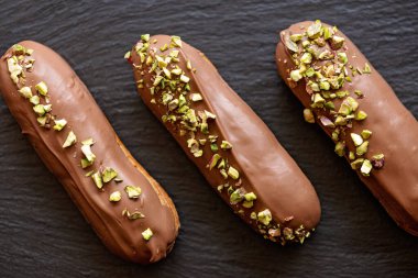 Fransız tatlı eklerleri ya da sütlü çikolata jöleli profiteroller ve siyah taş tabakta şam fıstığı. Kremalı ve soslu kekler. Yumuşak seçici odak.