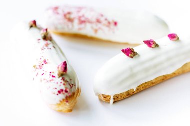 Fransız tatlı eklerleri ya da beyaz arka planda gül aromalı beyaz çikolata jöleli profiteroller. Kremalı, gül kremalı ve soslu hamur tatlısı. Yumuşak seçici odak.