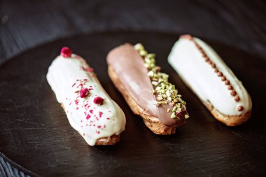 Fransız tatlı eklerleri ya da çikolata kremalı profiteroller ve siyah taş tabakta farklı malzemeler. Kremalı muhallebi kekleri. Yumuşak seçici odak.