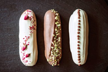 Fransız tatlı eklerleri ya da çikolata kremalı profiteroller ve siyah taş tabakta farklı malzemeler. Kremalı muhallebi kekleri. Yumuşak seçici odak.