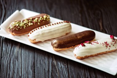 Fransız tatlı eklerleri ya da çikolata jöleli profiteroller, beyaz tabakta farklı malzemeler, ahşap arka plan. Kremalı muhallebi kekleri. Yumuşak seçici odak.