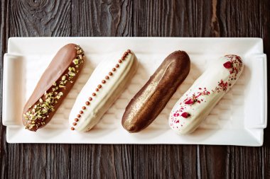 Fransız tatlı eklerleri ya da çikolata jöleli profiteroller, beyaz tabakta farklı malzemeler, ahşap arka plan. Kremalı muhallebi kekleri. Yumuşak seçici odak.