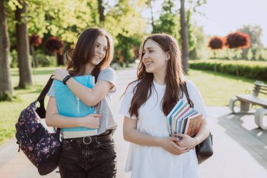 İki mutlu gülümseyen öğrenci kız, güneşli bir günde kampüste yürüyor ve birbirleriyle konuşuyorlar. Yumuşak seçici odak.