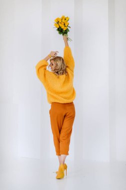 Stüdyoda beyaz bir arka planda poz veren, sarı güllerle dolu bir buketi olan mutlu genç sarışın kadın. Yumuşak seçici odak.