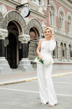 Beyaz takım elbiseli şık bir bayan zarif bir saç stili ve şehrin sokaklarında bir buket ortanca çiçeği var. Gelin olan kadın. Yumuşak seçici odak