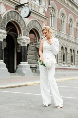 Beyaz takım elbiseli şık bir bayan zarif bir saç stili ve şehrin sokaklarında bir buket ortanca çiçeği var. Gelin olan kadın. Yumuşak seçici odak