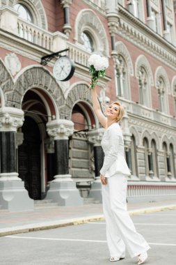 Beyaz takım elbiseli şık bir bayan zarif bir saç stili ve şehrin sokaklarında bir buket ortanca çiçeği var. Gelin olan kadın. Yumuşak seçici odak