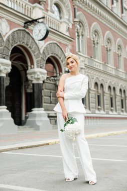 Beyaz takım elbiseli şık bir bayan zarif bir saç stili ve şehrin sokaklarında bir buket ortanca çiçeği var. Gelin olan kadın. Yumuşak seçici odak