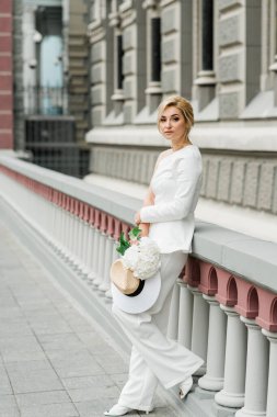 Beyaz takım elbiseli şık bir bayan zarif bir saç stili ve şehrin sokaklarında bir buket ortanca çiçeği var. Gelin olan kadın. Yumuşak seçici odak