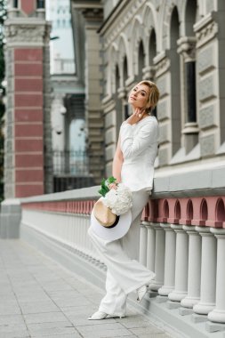 Beyaz takım elbiseli şık bir bayan zarif bir saç stili ve şehrin sokaklarında bir buket ortanca çiçeği var. Gelin olan kadın. Yumuşak seçici odak