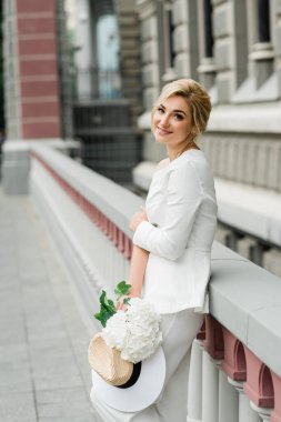 Beyaz takım elbiseli şık bir bayan zarif bir saç stili ve şehrin sokaklarında bir buket ortanca çiçeği var. Gelin olan kadın. Yumuşak seçici odak