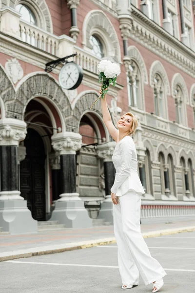 Beyaz takım elbiseli şık bir bayan zarif bir saç stili ve şehrin sokaklarında bir buket ortanca çiçeği var. Gelin olan kadın. Yumuşak seçici odak