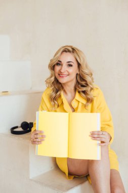 Sevimli, çekici, gülümseyen, sarı takım elbiseli, kulaklıklı ve sarı defterli çekici bir kadının portresi. Yumuşak seçici odak.