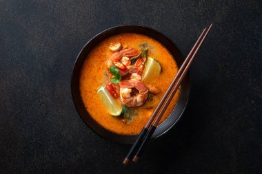 Tom Yum çorbası, karidesli, seramik, siyah kâseli, yemek çubuklu, siyah arka planda, üst manzaralı.