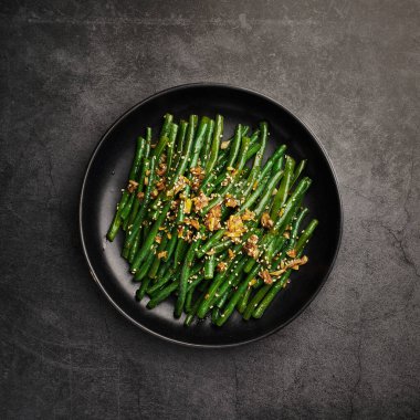 Siyah arka planda susamlı yeşil fasulye ve sarımsak.