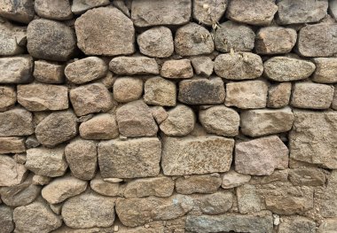 Zengin dokunsal dokusu ve arka planı olan düzensiz kayalardan yapılmış taştan bir duvar..