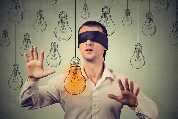 Blindfolded young man walking through light bulbs searching for bright idea — Stockfoto