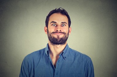 Crazy looking man making funny faces isolated on gray wall background clipart