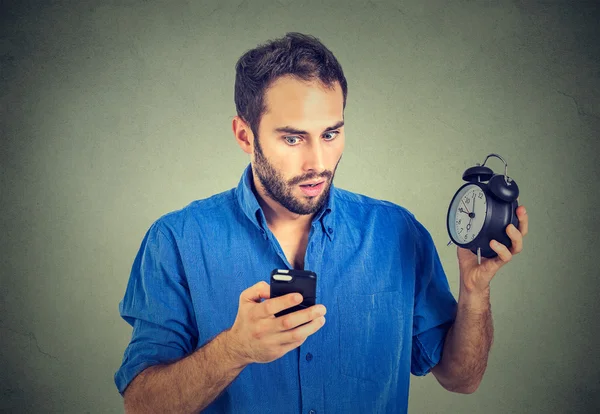 Perplex Business man met wekker kijken naar slimme telefoon — Stockfoto