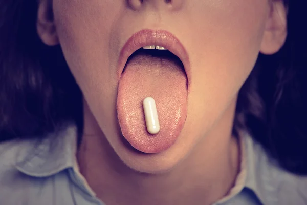 Closeup cropped image of young woman with white pill on her tongue — ストック写真