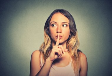 secretive young woman placing finger on lips asking shh, quiet