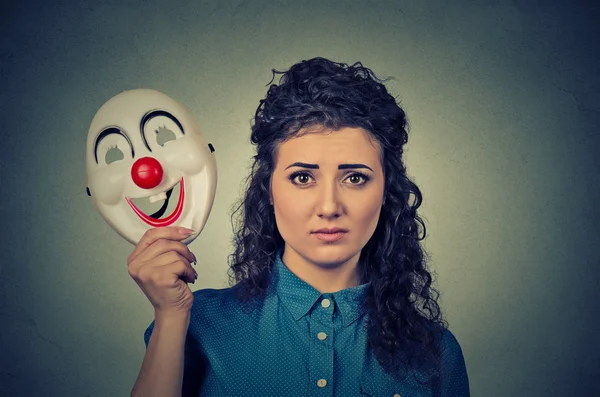 Расстроенная женщина с грустным выражением лица, держащая клоунскую маску, выражающую бодрость — стоковое фото