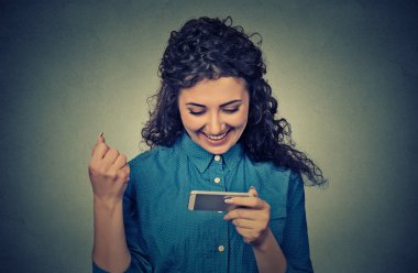 young woman looking at her mobile phone and smiling pumping fist celebrates success
