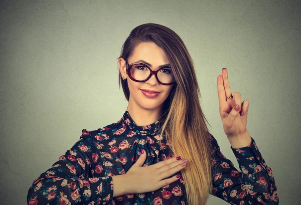 Молода жінка в окулярах робить обіцянку ізольовано на сірому фоні стіни — стокове фото