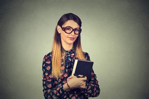 Young cheerful woman student in glasses standing and holding a book — Stok fotoğraf