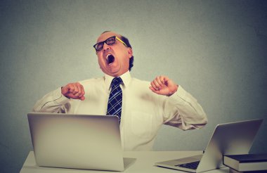 exhausted business man yawning at work in office sitting at his desk with laptop computers clipart