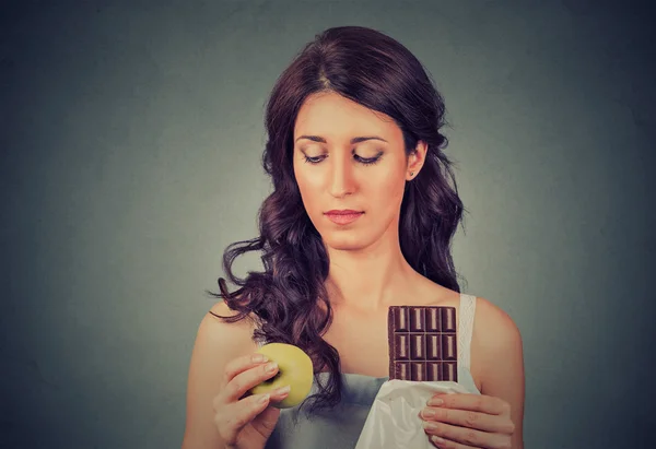 Mulher de aparência confusa com chocolate e maçã tentando fazer uma escolha saudável — Fotografia de Stock