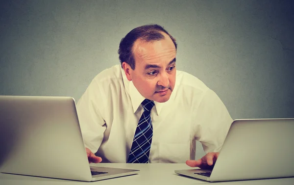 Hombre de negocios de mediana edad multitarea trabajando en dos computadoras en su oficina —  Fotos de Stock