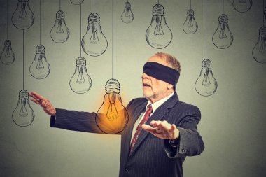 Blindfolded senior man walking through light bulbs searching for bright idea 
