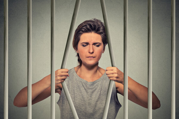 Stressed desperate sad woman bending bars of her prison cell