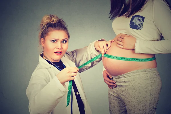 Mulher grávida expondo barriga enquanto um médico ginecologista chocado usa fita métrica para acompanhar o crescimento do bebê — Fotografia de Stock