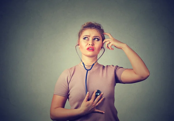 Mujer pensativa escuchando su corazón con estetoscopio — Foto de Stock