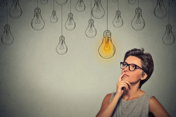 Portrait thinking woman in glasses looking up with light idea bulb above head — Stock Photo, Image
