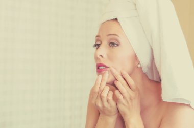 üzgün kadın yüzünde zit görmek için sinirli bir aynaya bakarak, sivilce