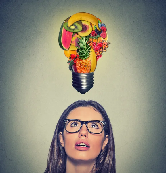 健康的なアイデアダイエットのヒントを食べる。頭の上の果物で作られた電球を見上げる女性 — ストック写真