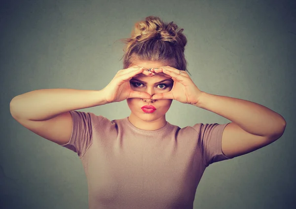 Unzufriedene junge Frau blickt durch Finger wie Ferngläser — Stockfoto