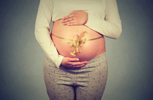 Střední část těhotné ženy s obalenou stuhou na břiše — Stock fotografie