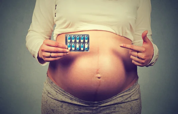 Close up imagem recortada mulher grávida com grande barriga apontando para pílulas — Fotografia de Stock