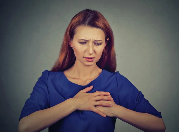 Mujer joven con dolor en el pecho tocando el pecho aislado sobre fondo de pared gris — Foto de Stock