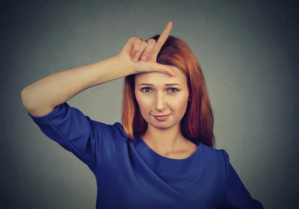 Woman giving loser sign on forehead, looking at you — Stockfoto