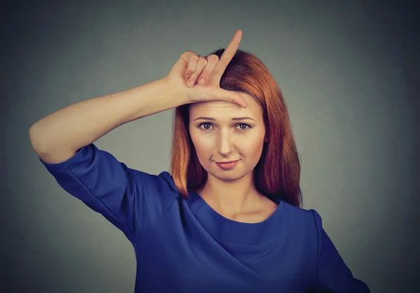 Woman giving loser sign on forehead, looking at you — Zdjęcie stockowe