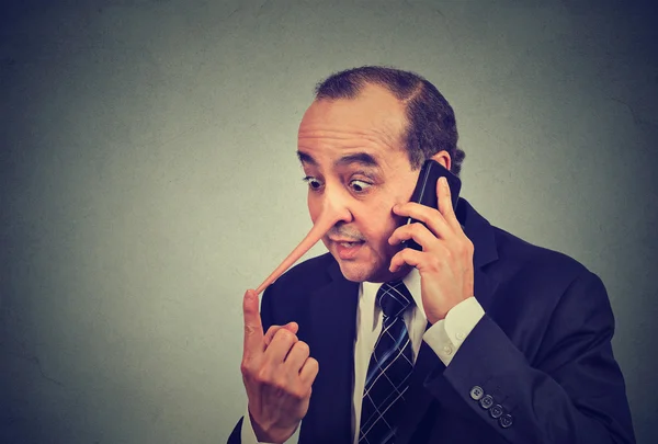 Lügner Kundendienstmitarbeiter. Mann mittleren Alters mit langer Nase, der auf einem Mobiltelefon spricht, das isoliert vor grauem Hintergrund liegt. Lügenkonzept. menschlicher Gesichtsausdruck Emotion Gefühl Charakterzüge — Stockbild Lügner Kundendienstmitarbeiter. Mann mit langer Nase spricht auf Handy liegend — Stockfoto