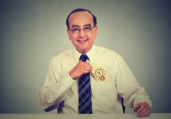 Kreativer Geschäftsmann mittleren Alters mit einer tollen Idee, eine Karte mit einer handgezogenen Glühbirne aus seiner Hemdtasche zu ziehen, Retro-Filtereffekt aufgetragen. Geschäftsmann mit Idee sitzt an seinem Bürotisch — Stockbild Geschäftsmann mit toller Idee zieht Karte mit Glühbirne aus Hemdtasche — Stockfoto