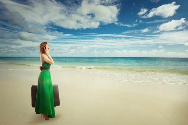 Beautiful woman traveler at the beach with suitcase talking on mobile phone — Stock Photo, Image