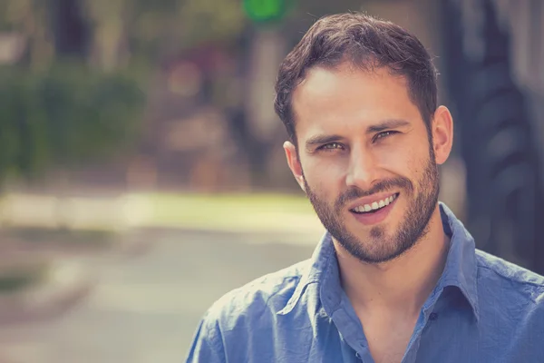 Um homem feliz. Bonito cara na camisa casual sorrindo de pé contra o fundo urbano da cidade — Fotografia de Stock